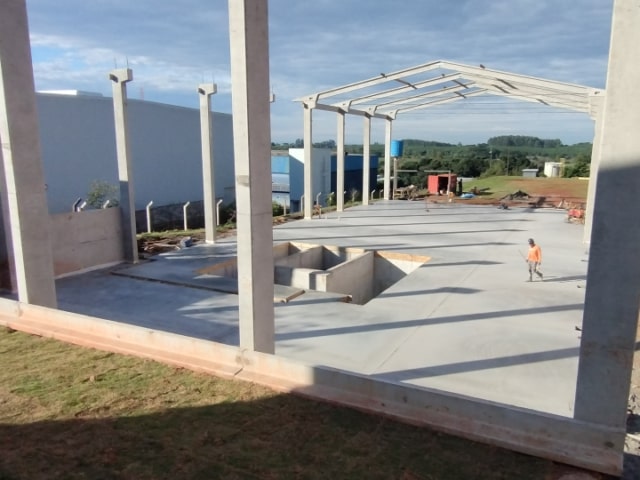 Vista geral da obra mostrando a estrutura do galpão e o piso de concreto industrial concluído.